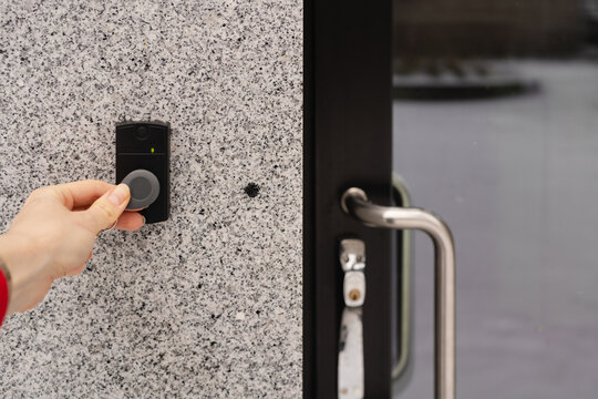 Close-up of a female hand holding a keychain with a key fob near a key reader access device on a building&rsquo;s exterior wall, showcasing modern security, smart access, and contactless entry technology