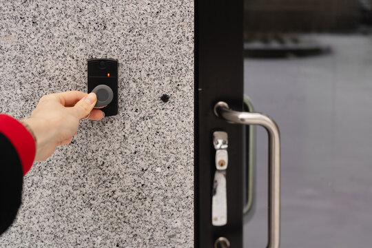 Close-up of a female hand holding a keychain with a key fob near a key reader access device on a building&rsquo;s exterior wall with door. modern security, smart access, and contactless entry technology