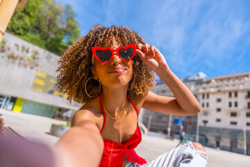 Playful cool woman with hear shape sunglasses taking selfie outdoors