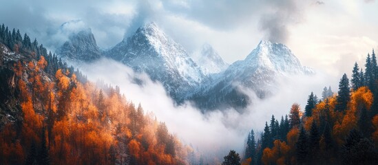 Dramatic mountain landscape featuring snowy peaks under a gray cloudy sky with autumn-colored forest in the foreground and fog rolling through.