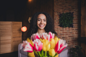 Fototapeta premium Young woman with flowers smiling indoors surrounded by natural light in a cozy home environment