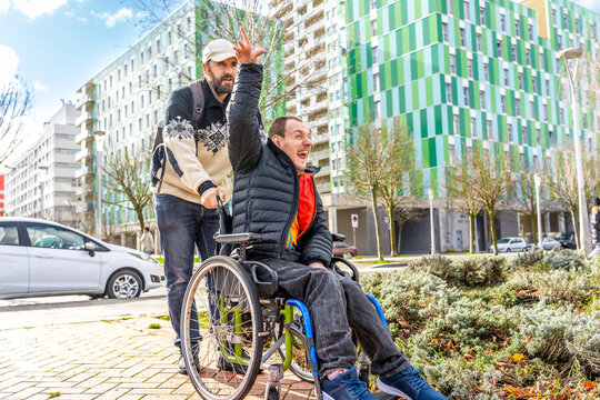 Caregiver pushing happy disabled man in wheelchair in city