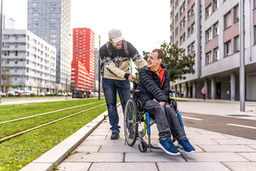 Volunteer pushing young disabled man in wheelchair in city