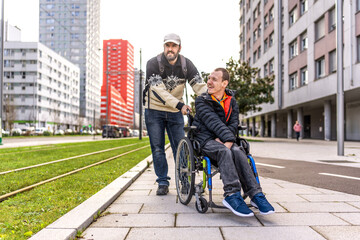 Man pushing friend in wheelchair on city sidewalk