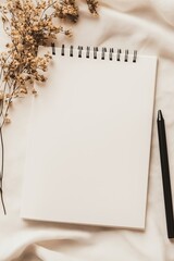 Blank notebook and pen on a soft beige background with dried flowers nearby
