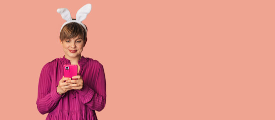A beautiful girl with bunny ears on a colored background with a smartphone in her hands.