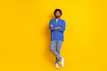 Young stylish man wearing a casual blue polo shirt, standing with arms crossed on a vibrant yellow...