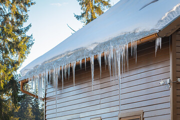 Long icicles are hanging from the roof of a house © Menyhert