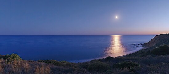 Obraz premium Tranquil twilight ocean scene featuring a soft blue color palette with the moon reflecting on calm waters creating a serene atmosphere.