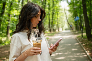 Woman walking in the summer park ,drinking coffee ,looking  her phone