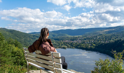 Traveler woman sitting on a bench high above a blue lake with stunning panoramic view 