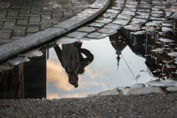 Reflection of a Woman and Cityscape in a Puddle