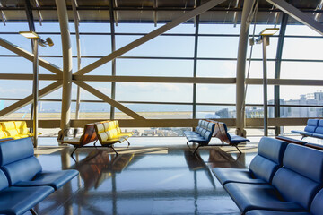 Empty multiple rows of seats  with a large window view of blurry runway and an airplane background in seating area of airport terminal. Bright sunlight casting shadows on the floor. Vacation concept.