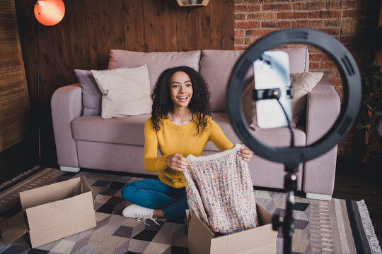 Young african american woman unpacking sweater in cozy living room for online unboxing video