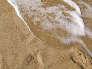 Fototapeta premium Gentle waves rolling onto sandy beach at sunrise, creating bubbles and a shimmering surface