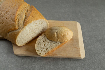 A freshly baked loaf of bread with a golden crust is placed on a wooden cutting board.