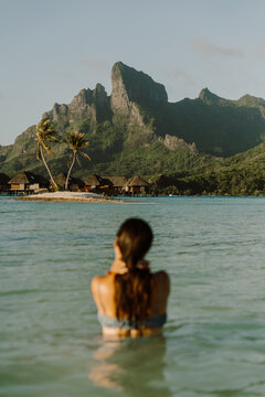A woman enjoys the crystal-clear waters of Bora Bora, gazing at the lush green mountains and overwater bungalows. A dreamy escape to tropical paradise, where relaxation and adventure meet