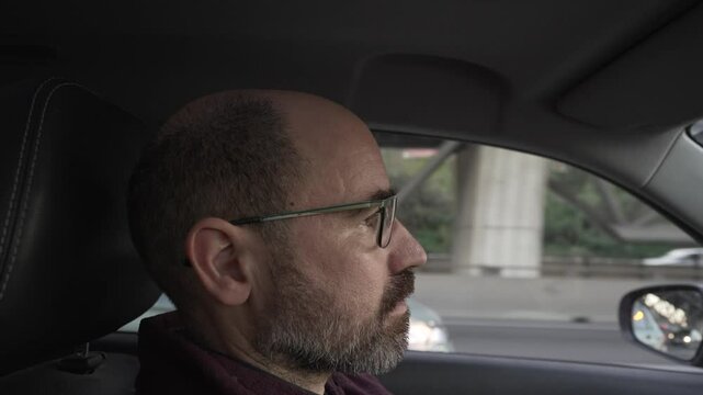driver profile, man in his forties, bald with glasses. Attentive to driving