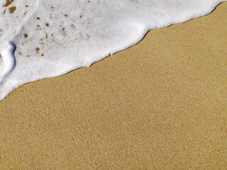 Stunning close-up of ocean wave foam gently lapping onto golden sand. Perfect for travel, summer, or beach-themed designs