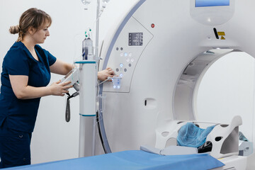 A medical nurse, doctor push buttons of a modern CT scanner while attending to a patient in a...