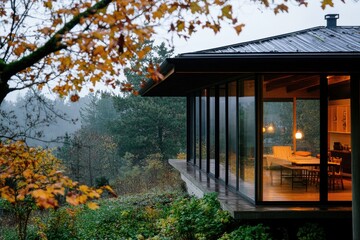 Autumnal view of a modern house with large windows overlooking a lush forest.