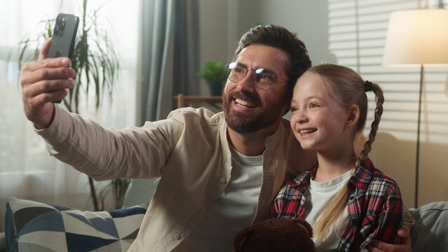 Caucasian happy family make selfie photo with mobile phone at home smiling posing together man male dad father face mask digital app online gadget with little girl daughter child kid video call vlog