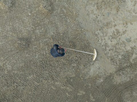 Aerial view of traditional salt farmers working alone in the salt farms in Indonesia. An old Asian salt farmers working hard in the salt farms - Powered by Adobe