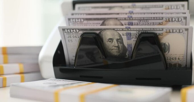 Currency counting machine processes stack of hundred dollar bills. Precision banking technology with additional banknote pack in bank slow motion