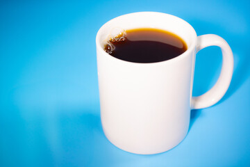 A cup of coffee with milk in a white mug placed on a bright blue background. The perfect combination for breakfast or a snack.