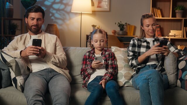 Family mother father daughter girl kid child parents man woman relaxing in home night evening on couch using mobile phones apps social media scrolling smartphones gadgets addiction dependency overuse