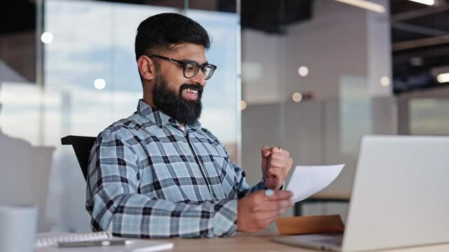 Excited businessman opens envelope, reads good news, and celebrates success in modern office. Business man in office open paper envelope received bank loan approval profitable proposition opportunity.