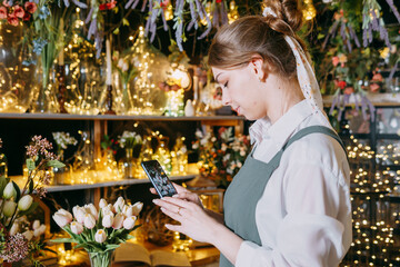 A woman in her florist shop collects bouquets of flowers. The concept of a small business. Bouquets of tulips for the holiday on March 8.