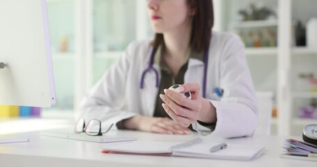 Doctor squishes small soccer ball in hand sitting at desk. Young medical specialist reduces stress with soft toy working in healthcare setting