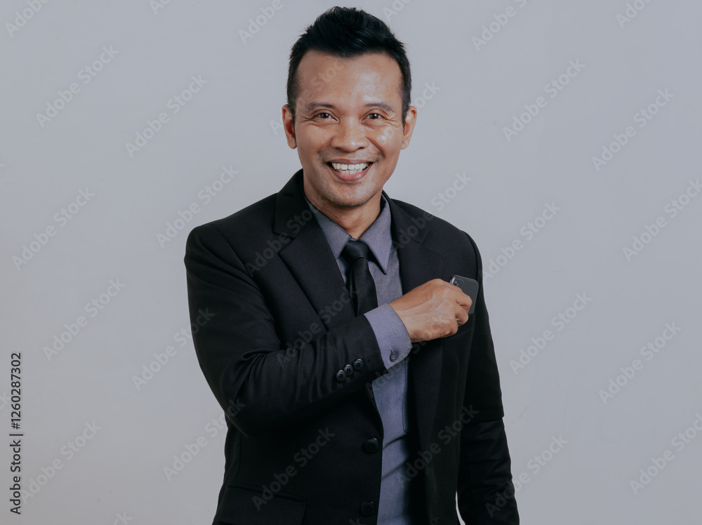 Wall mural Asian boss manager businessman smiling looking to camera while putting his mobile phone to his suit pocket, isolated over white background.