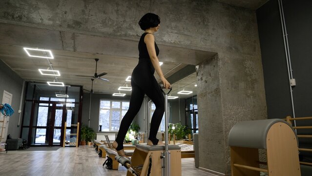 Woman performing Pilates step-up exercise on reformer in gym