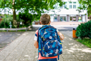 Happy little kid boy with satchel. Schoolkid on the way to middle or high school. Healthy adorable child outdoors on school yard. Back to school. Building on background.