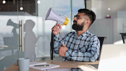 Bearded businessman in glasses speaks into megaphone in modern office. Male makes announcement to colleagues at business meeting. - Powered by Adobe