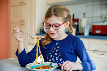 Little school girl eat pasta spaghetti with tomato bolognese with minced meat. Happy preschool...