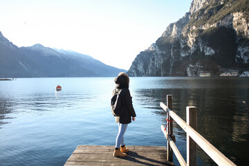 A traveler in winter clothing stands on a wooden dock overlooking a serene mountain lake.  Amazing...