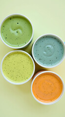 A symmetrical top-down view of colorful milk shakes in green, blue, orange, and yellow arranged in a neat triangle on a clean, pale background