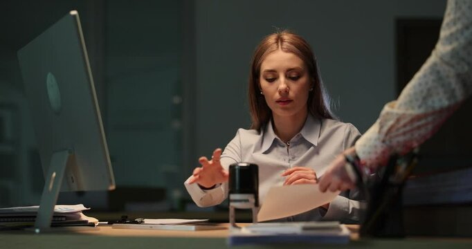 Serious businesswoman places stamp on important document in semi dark room. Female reviews final details of contract and signs document. Slow motion