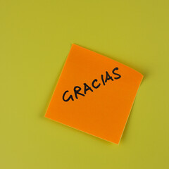 Gracias, thank you in spanish, written in black capital letters on an orange sticky note against a yellow background