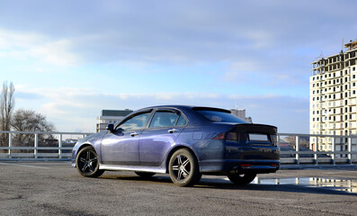 Dark blue car parked in a parking lot with a building under construction in the background.