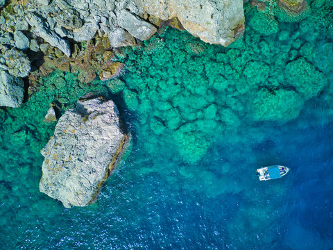 Zingaro Nature Reserve coastline with a small boat in the crystal clear waters seen from above