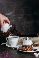 Coffee in a white cup with chocolate flowers hand pours milk from milkweed freeze drops black background	