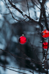 red Christmas tree decorations hanging on a tree under the snowfall, Christmas toys, red balls on...