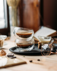 Coffee in glass cup on wooden background, espresso coffee in double-bottomed glass cups, cane sugar, open book, coffee on a black tray, lunch break, coffee still life close-up