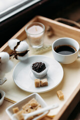 morning coffee  in a white cup with handmade chocolate candies, espresso, americano, breakfast on a wooden tray on the windowsill, brown sugar, candy, coffee in bed, cotton flowers, candles, romance