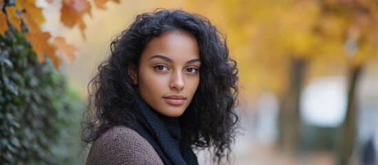 Young woman with curly hair standing in autumn park alley surrounded by colorful leaves and empty space for text or design.