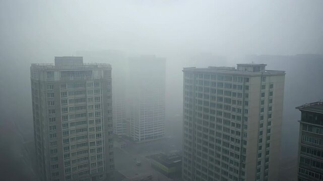 Aerial polluted Chinese city footage, tall buildings covered in thick heavy fog/smog. bird's-eye view. intense air pollution. Man-made smog derived from coal combustion, industrial emissions.